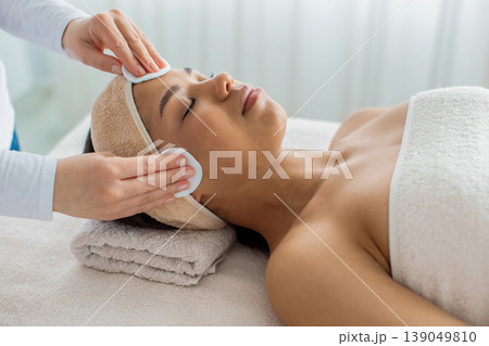 Spa therapist doing facial cleansing treatment with cotton pads to black woman Spa therapist doing facial cleansing treatment with cotton pads to black woman 139049810