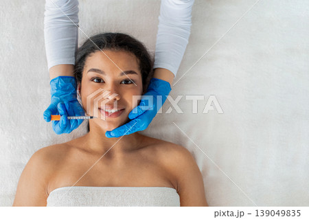 Young black woman receiving lip injection at modern spa salon, top view Young black woman receiving lip injection at modern spa salon, top view 139049835