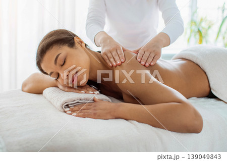 Young African American woman enjoying relaxing back massage at luxury spa salon Young African American woman enjoying relaxing back massage at luxury spa salon 139049843