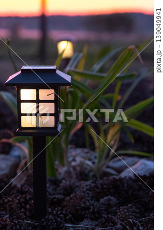 Asian-style solar lantern in flowerbed with grasses, pebbles and perennials, eco-friendly garden lighting, evening landscape mood. Asian-style solar lantern in flowerbed with grasses, pebbles and perennials, eco-friendly garden lighting, evening landscape mood. 139049941