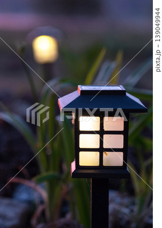 Japanese-inspired garden lantern, solar powered, surrounded by grasses and mulch, contemporary landscape, energy efficient flowerbed light. Japanese-inspired garden lantern, solar powered, surrounded by grasses and mulch, contemporary landscape, energy efficient flowerbed light. 139049944