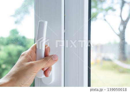 Finger on window handle, opening for ventilation, plastic hardware, airing room, cross-draft and fresh air, modern frame, household care, security. 139050018