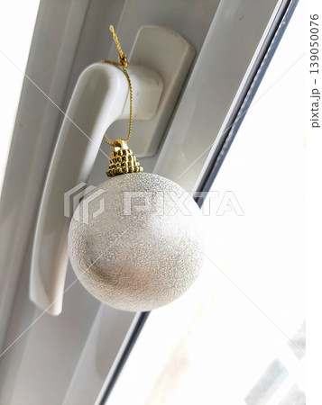 Silver Christmas bauble hanging on a white plastic window handle. Silver Christmas bauble hanging on a white plastic window handle. 139050076