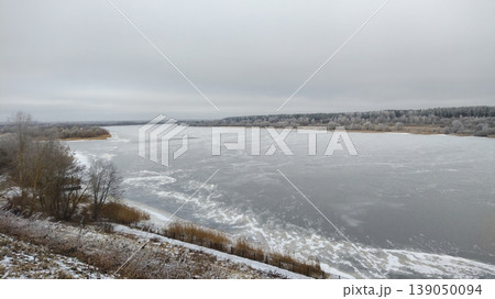 Frozen wide river covered with thin ice and snow under a cloudy winter sky. Frozen wide river covered with thin ice and snow under a cloudy winter sky. 139050094