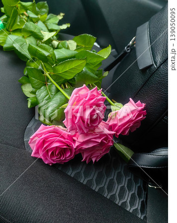 Bouquet of beautiful pink roses lying on a dark car seat next to a black leather bag. 139050095