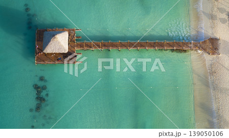 Drone shot of a small hut on a wooden pier on sandy beach with turquoise water 139050106