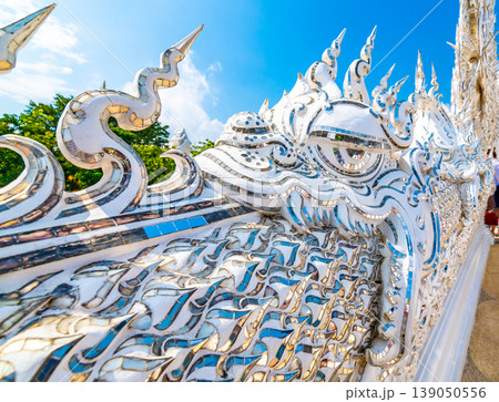 The white temple (Wat Rong Khun) in Chiang Rai city, Thailand. Beautiful buddhist ancient building with bridge above damned souls of sinners, path to the heaven. Famous tourist destination. Blue sky The white temple (Wat Rong Khun) in Chiang Rai city, Thailand. Beautiful buddhist ancient building with bridge above damned souls of sinners, path to the heaven. Famous tourist destination. Blue sky 139050556