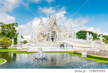 The white temple (Wat Rong Khun) in Chiang Rai city, Thailand. Beautiful buddhist ancient building with bridge above damned souls of sinners, path to the heaven. Famous tourist destination. Blue sky 139050563