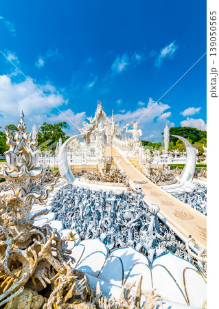 The white temple (Wat Rong Khun) in Chiang Rai city, Thailand. Beautiful buddhist ancient building with bridge above damned souls of sinners, path to the heaven. Famous tourist destination. Blue sky 139050565