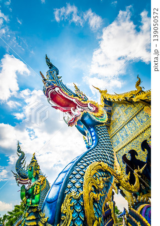 Statue of dragon at Wat Rong Suea Ten temple (blue temple) near Chiang Rai city, Thailand. Mystical sculpture of ancient beast. View from bottom with blue sky dynamic background 139050572