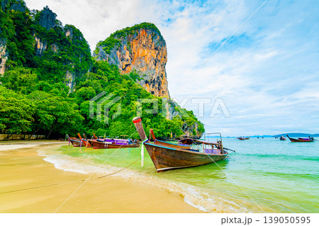 The famous Railay beach at Krabi, Thailand. Long tailed boats are prepared for passengers near limestone rock. Tropical paradise, famous tourist destination. Turquoise sea with white sand The famous Railay beach at Krabi, Thailand. Long tailed boats are prepared for passengers near limestone rock. Tropical paradise, famous tourist destination. Turquoise sea with white sand 139050595