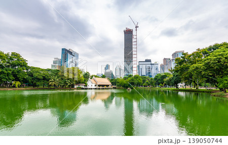 Bangkok cityscape view from Lumpini park in city center. Panoramic photo of skyscrapers and futuristic buildings from metal and glass. View from the small lake in Lumpini park. Fresh green plants. Bangkok cityscape view from Lumpini park in city center. Panoramic photo of skyscrapers and futuristic buildings from metal and glass. View from the small lake in Lumpini park. Fresh green plants. 139050744