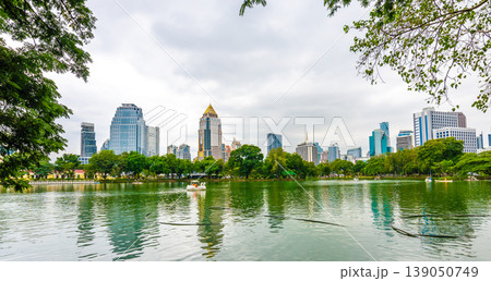 Bangkok cityscape view from Lumpini park in city center. Panoramic photo of skyscrapers and futuristic buildings from metal and glass. View from the small lake in Lumpini park. Fresh green plants. Bangkok cityscape view from Lumpini park in city center. Panoramic photo of skyscrapers and futuristic buildings from metal and glass. View from the small lake in Lumpini park. Fresh green plants. 139050749