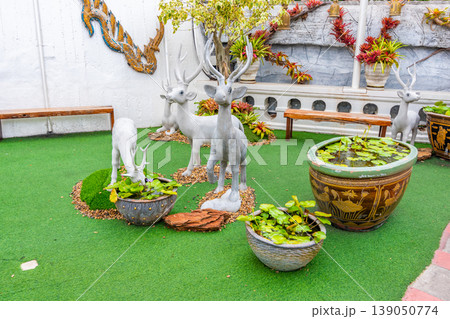 Small deer statues with white color placed on green ground. Waterlily in the pot. 139050774