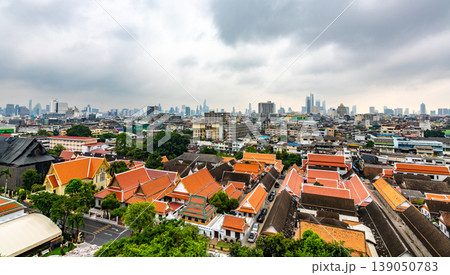 Panorama view of Bangkok city, Thailand. Cityscape of residental buildings in foreground, temples, skyscrapers and modern buildings in far. Fresh trees and plants. Cloudy weather, dramatic clouds. 139050783