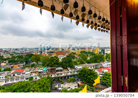 Look from window in Wak Saket temple (Golden mount) in Bangkok city, Thailand. Wooden ancient window with historic frame and heart bells shape. In far the cityscape of Bangkok. Religion, buddhism Look from window in Wak Saket temple (Golden mount) in Bangkok city, Thailand. Wooden ancient window with historic frame and heart bells shape. In far the cityscape of Bangkok. Religion, buddhism 139050784