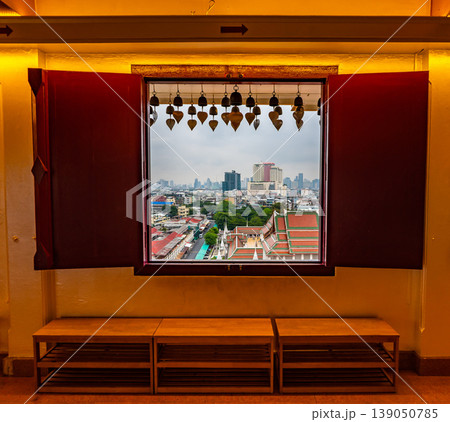 Look from window in Wak Saket temple (Golden mount) in Bangkok city, Thailand. Wooden ancient window with historic frame and heart bells shape. In far the cityscape of Bangkok. Religion, buddhism 139050785