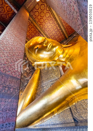 Beautiful statue of reclining golden Buddha placed in Wat Pho temple, Bangkok. Spiritual place of buddhism religion with beautiful ornaments on the pillar. Detail view of Buddha's head 139050819
