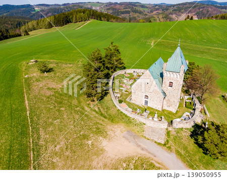 Aerial view of St Michael chapel in czech republic. Chapel is one of the oldest church in country. Fresh agriculture land with small village in background. Beautiful stone religion building, heritage. Aerial view of St Michael chapel in czech republic. Chapel is one of the oldest church in country. Fresh agriculture land with small village in background. Beautiful stone religion building, heritage. 139050955