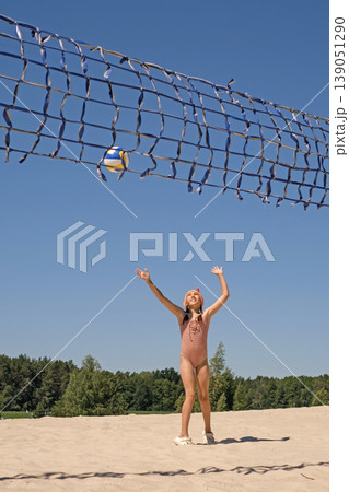 A girl in a swimsuit serves a ball in a volleyball game on the beach by the sea. Active sports activities during the summer holidays. A girl in a swimsuit serves a ball in a volleyball game on the beach by the sea. Active sports activities during the summer holidays. 139051290