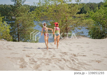 Children in swimsuits run to the lake to swim in the water on a hot summer vacation day. Girls in bright leopard print Swimwear Children in swimsuits run to the lake to swim in the water on a hot summer vacation day. Girls in bright leopard print Swimwear 139051293