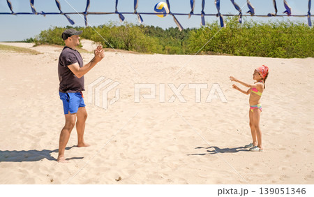 The father teaches the child to hit the ball. Beach volleyball. A girl in a swimsuit plays with her dad 139051346