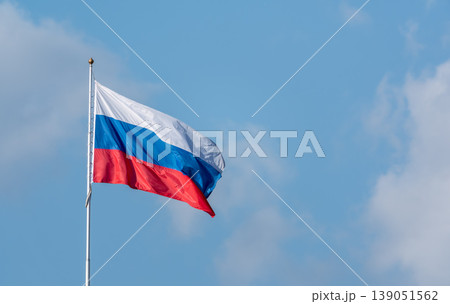 Russian tricolor flag waving in the wind against a blue sky. Fieldbird sits on a branch in spring with a blurred background. Russian tricolor flag waving in the wind against a blue sky. Fieldbird sits on a branch in spring with a blurred background. 139051562