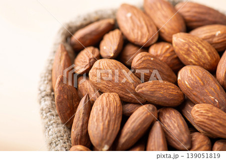 Top view of almonds in small bag. Close up shot of fresh tasty almond nuts in bag made of linen fiber on light background Top view of almonds in small bag. Close up shot of fresh tasty almond nuts in bag made of linen fiber on light background 139051819