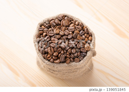Small bag of roasted coffee beans. Top down shot of aromatic coffee grain in sack on wooden table Small bag of roasted coffee beans. Top down shot of aromatic coffee grain in sack on wooden table 139051845