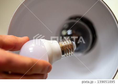 Close up of menhand holding LED light bulb, going to place in into the lamp. Upgrading your home's lighting with energy-efficient light bulb 139051895