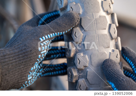 Male hands in gloves examine the worn Enduro motorcycle tires. Two-wheeled vehicle, which has been in a lot of use, tires need to be replaced 139052006