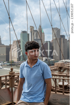 New york, usa august 15,2024. Young man standing on brooklyn bridge, gazing across east river at manhattan skyline on a clear summer day, urban sightseeing 139052187