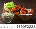 Spicy Buffalo wings with blue cheese sauce and celery sticks in paper tray on a wooden table. crunchy buffalo chicken wings with celery sticks and blue cheese dipping sauce on a wooden table. 139052228