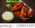 Spicy Buffalo wings with blue cheese sauce and celery sticks in paper tray on a wooden table. crunchy buffalo chicken wings with celery sticks and blue cheese dipping sauce on a wooden table. 139052229
