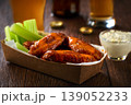 Buffalo BBQ chicken wings with blue cheese sauce and beer with of celery sticks in a paper container on a wooden table.Buffalo chicken wings in a disposable tray and beer on a wooden table 139052233