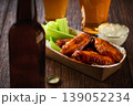 Buffalo BBQ chicken wings with blue cheese sauce and beer with of celery sticks in a paper container on a wooden table.Buffalo chicken wings in a disposable tray and beer on a wooden table 139052234