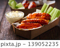 Spicy Buffalo wings with blue cheese sauce and celery sticks in paper tray on a wooden table. crunchy buffalo chicken wings with celery sticks and blue cheese dipping sauce on a wooden table. 139052235
