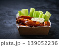Buffalo chicken wings in a disposable tray on a dark table, selective focus.Buffalo BBQ chicken wings with celery sticks and chunky blue cheese dressing in a paper container on a dark table. 139052236