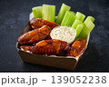 Buffalo chicken wings in a disposable tray on a dark table, selective focus.Buffalo BBQ chicken wings with celery sticks and chunky blue cheese dressing in a paper container on a dark table. 139052238