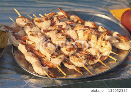 Grilled shrimp skewers on metal plate, light char, juicy texture served in outdoor street food setting. Seafood cooking, shrimp skewers, barbecue grill, protein meal street food Grilled shrimp skewers on metal plate, light char, juicy texture served in outdoor street food setting. Seafood cooking, shrimp skewers, barbecue grill, protein meal street food 139052585
