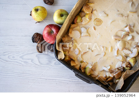 Apple pie batter poured over sliced apples in a baking pan, with rustic background, alongside fresh apples and walnuts. Apple pie batter poured over sliced apples in a baking pan, with rustic background, alongside fresh apples and walnuts. 139052964