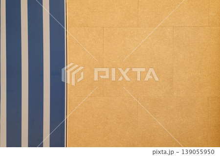 Abstract architectural background featuring bold blue vertical stripes alongside a textured orange tiled surface. Minimalist interior design detail highlighting geometric patterns and contrast. Abstract architectural background featuring bold blue vertical stripes alongside a textured orange tiled surface. Minimalist interior design detail highlighting geometric patterns and contrast. 139055950