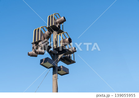 A tall industrial light pole with multiple spotlights and floodlights mounted on a metal structure against a clear blue sky. Professional outdoor lighting equipment for events or public spaces. 139055955