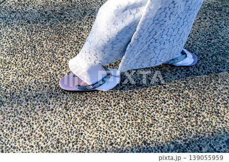 view of person wearing traditional Japanese tabi socks and purple zori sandals walking on a pebble stone path. Part of a light blue lace kimono is visible. Cultural fashion shot. view of person wearing traditional Japanese tabi socks and purple zori sandals walking on a pebble stone path. Part of a light blue lace kimono is visible. Cultural fashion shot. 139055959