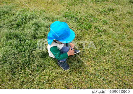 草むらの中に座る水色のカラー帽子の子供 草むらの中に座る水色のカラー帽子の子供 139058000