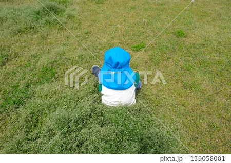 草むらの真ん中に座る水色カラー帽子の子供 草むらの真ん中に座る水色カラー帽子の子供 139058001
