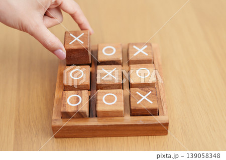 Hand holding and playing wooden block of tic tac toe game. A completed game of noughts and crosses or Xs and Os game. Challenge, Competition, winning, tactic, strategy and recreation concepts Hand holding and playing wooden block of tic tac toe game. A completed game of noughts and crosses or Xs and Os game. Challenge, Competition, winning, tactic, strategy and recreation concepts 139058348