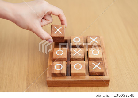 Hand holding and playing wooden block of tic tac toe game. A completed game of noughts and crosses or Xs and Os game. Challenge, Competition, winning, tactic, strategy and recreation concepts Hand holding and playing wooden block of tic tac toe game. A completed game of noughts and crosses or Xs and Os game. Challenge, Competition, winning, tactic, strategy and recreation concepts 139058349