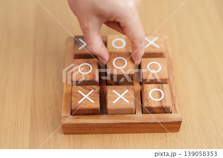 Hand holding and playing wooden block of tic tac toe game. A completed game of noughts and crosses or Xs and Os game. Challenge, Competition, winning, tactic, strategy and recreation concepts Hand holding and playing wooden block of tic tac toe game. A completed game of noughts and crosses or Xs and Os game. Challenge, Competition, winning, tactic, strategy and recreation concepts 139058353