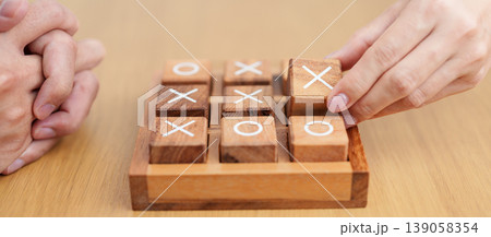 Hand holding and playing wooden block of tic tac toe game. A completed game of noughts and crosses or Xs and Os game. Challenge, Competition, winning, tactic, strategy and recreation concepts Hand holding and playing wooden block of tic tac toe game. A completed game of noughts and crosses or Xs and Os game. Challenge, Competition, winning, tactic, strategy and recreation concepts 139058354